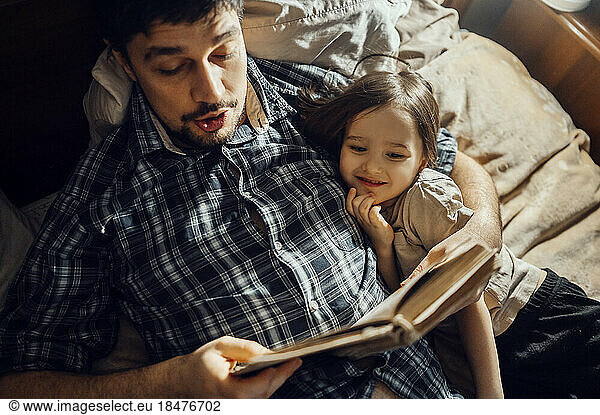 Father reading story book lying with son on bed
