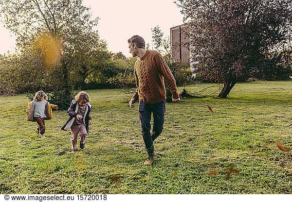 Father running with daughters on a meadow in autumn