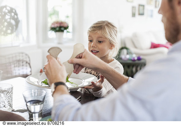 Father serving salad to daughter at dining table