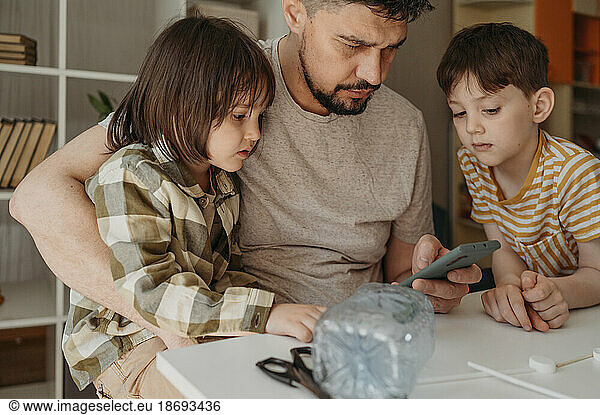 Father sharing smart phone with sons at home