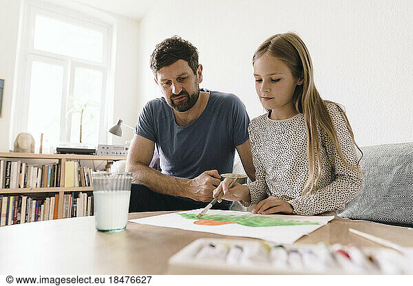 Father sitting by daughter painting on paper at home