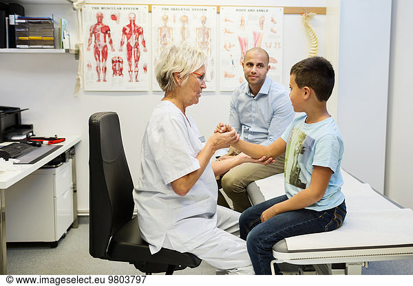 Father sitting by son being examined by orthopedic surgeon in clinic