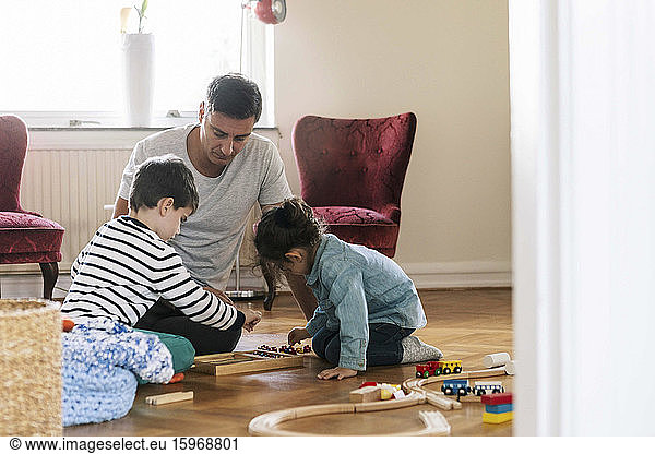 Father sitting while children playing in living room at home