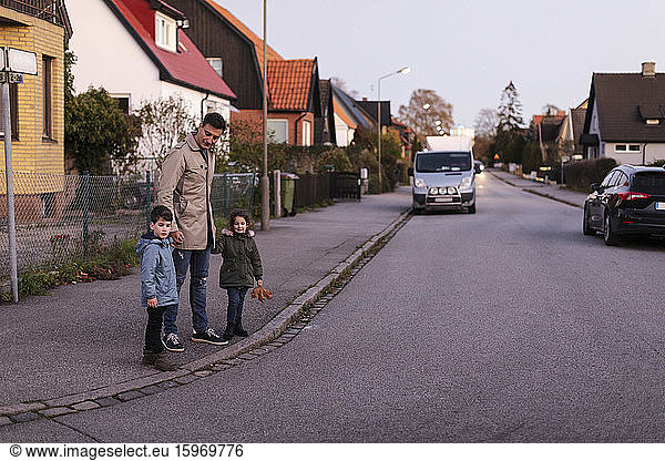 Father standing with children on sidewalk during autumn