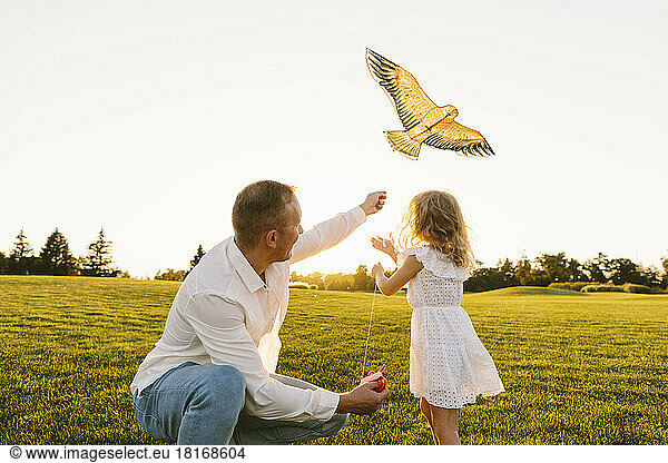 Father teaching daughter to fly kite at sunset