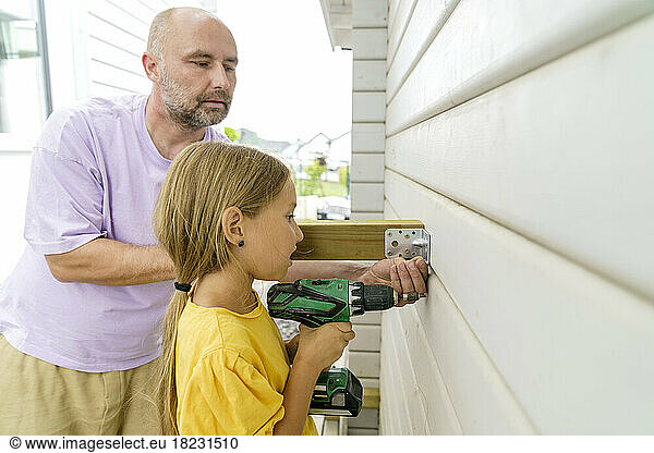 Father teaching daughter to work with screwdriver near wooden wall by house