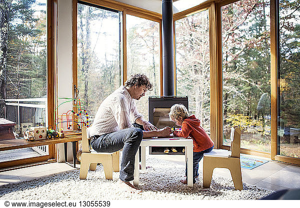 Father teaching son to write while sitting at chair in home