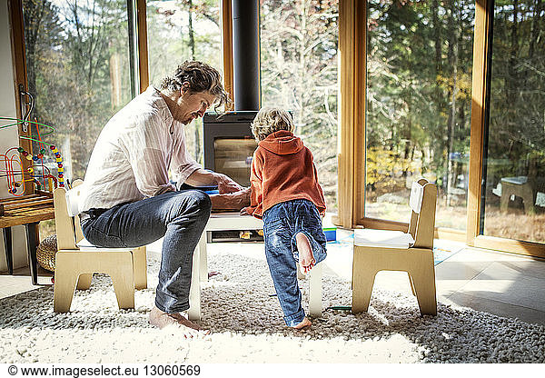 Father teaching son to write while sitting on chair at home