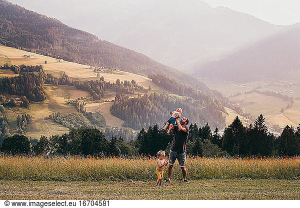 Father throwing baby in the air with mountains in the back in summer