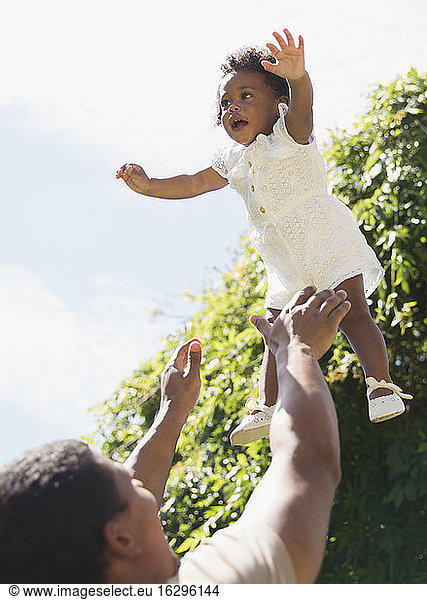 Father throwing daughter overhead playfully in sunshine