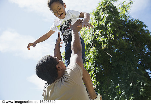 Father throwing son playfully overhead in sunshine