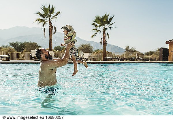 Father throwing young boy up in air while playing in pool on vacation