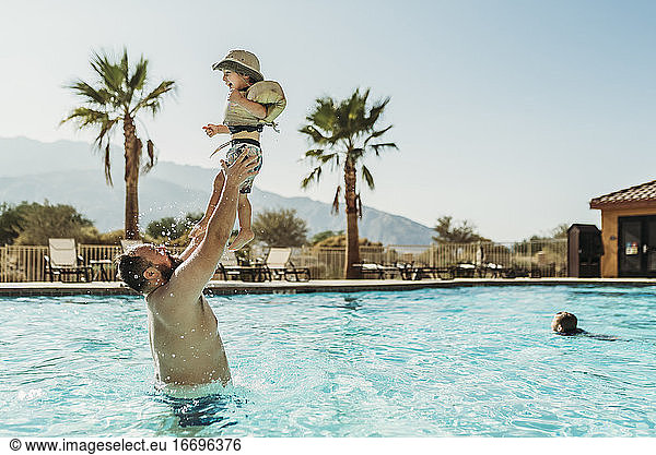 Father throwing young boy up in air while playing in pool on vacation
