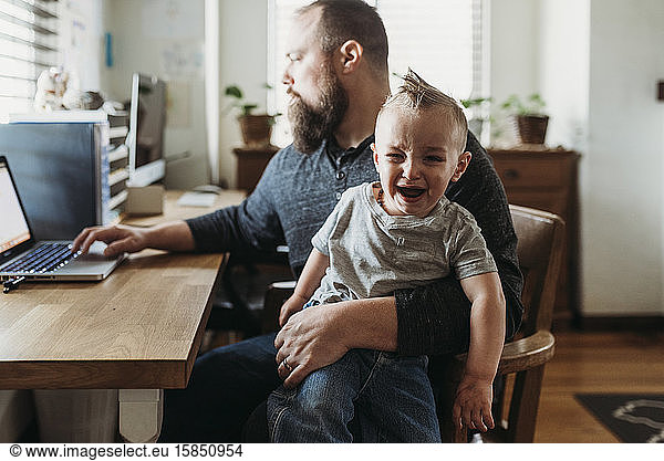 Father trying to work from home with toddler screaming in his lap