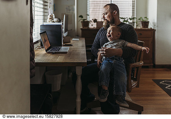 Father trying to work from home with toddler tantrum in his lap
