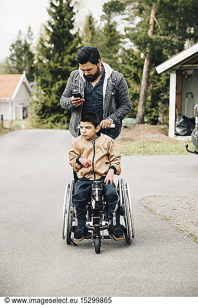 Father using smart phone while pushing autistic son on wheelchair
