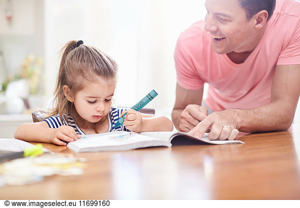 Father watching daughter coloring with crayon and coloring book at table