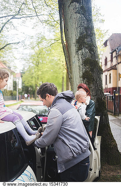 Father wearing shoes to daughter sitting on car
