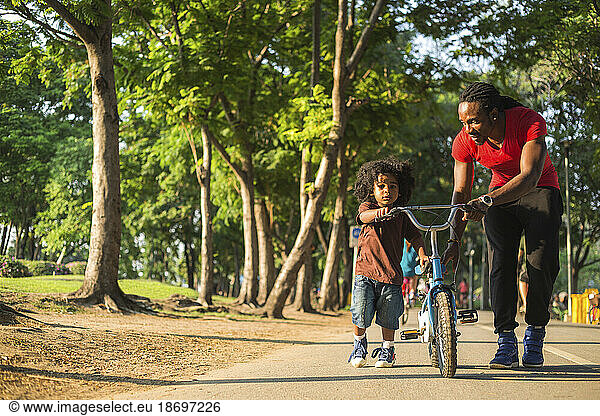 Father wheeling bicycle with son on footpath at park