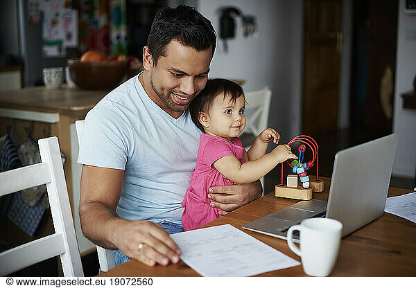 Father with baby girl using laptop on table at home
