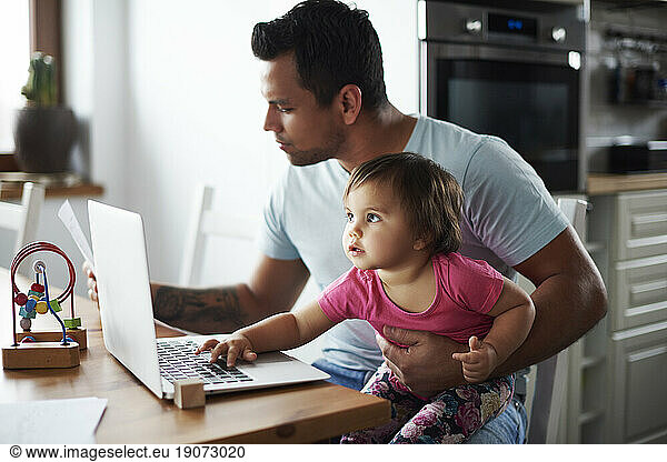 Father with baby girl using laptop on table at home