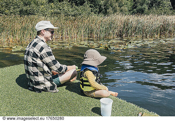 Father with baby son fishing in river on sunny day