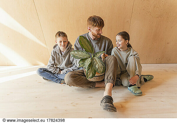 Father with children sitting in wooden house holding potted plant