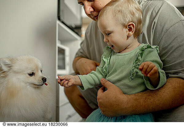 Father with cute daughter feeding dog at home
