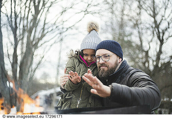 Father with daughter warming hands by fire during winter