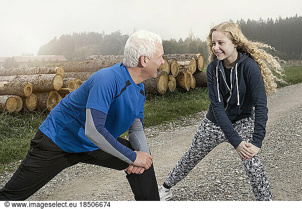 Father with his daughter stretching legs on footpath and smiling during dawn  Bavaria  Germany