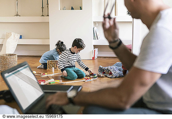 Father with laptop looking at children playing at home