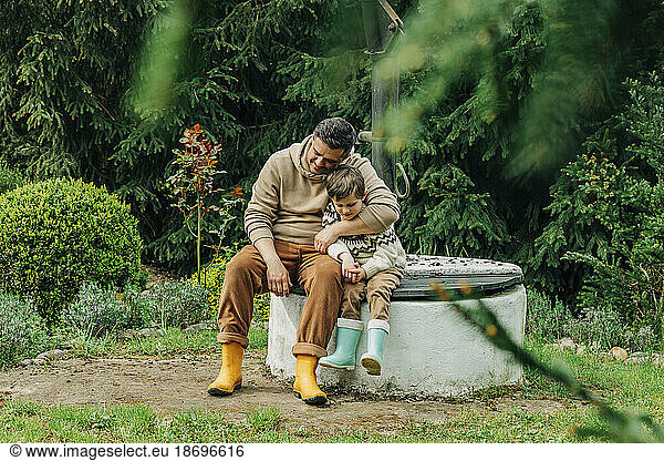 Father with son sitting together on well in garden
