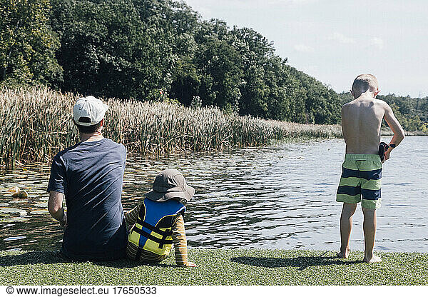 Father with sons at riverbank sitting on sunny day
