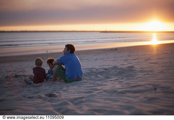 Father with two kids sitting on beach during sunset  Viana do Castelo  Norte Region  Portugal