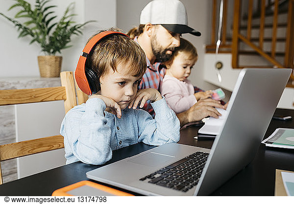 Father working at home using laptop with his children on his lap