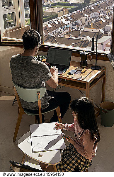 Father working on laptop while his daughter doing homework