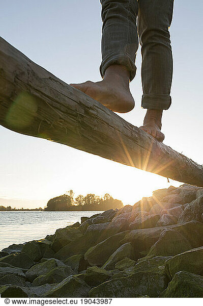 Feet balancing on log above river at sunrise