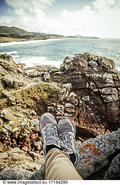Feet of a man sitting on top of the cliff overlooking the sea
