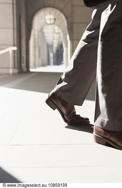 Feet of corporate businessman walking in sunny cloister