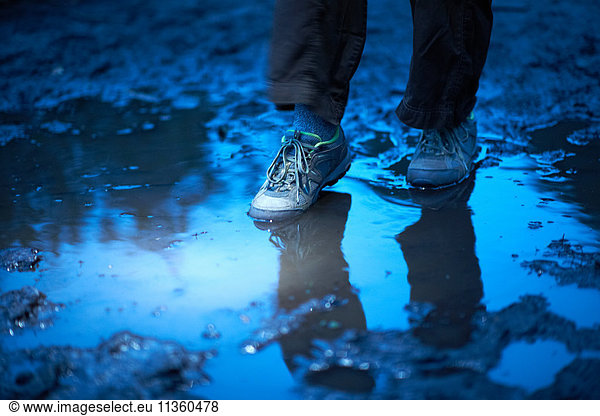 Feet of female hiker stepping in muddy puddle