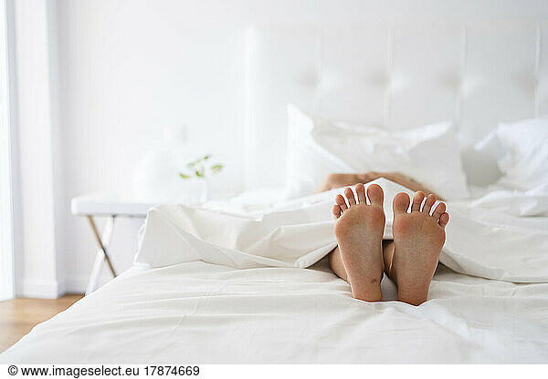 Feet of girl under blanket in bed