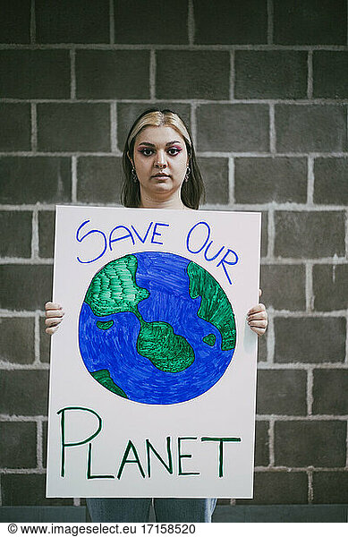 Female activist with planet earth poster standing against wall