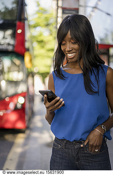 Female Afro-American using smartphone at bus stop in London  United Kingdom