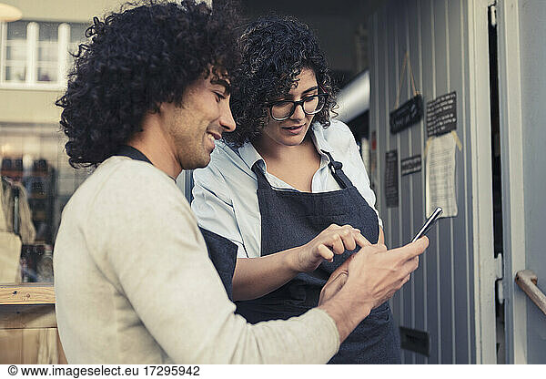 Female and male entrepreneurs using mobile phone while standing at doorway