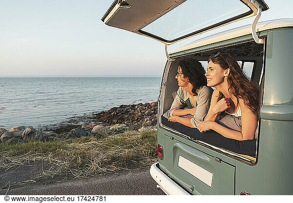 Female and male friends looking at sea from camping van during road trip