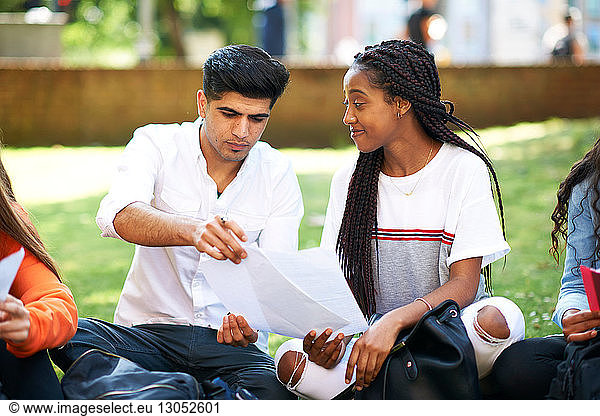 Female and male higher education students discussing paperwork on college campus lawn