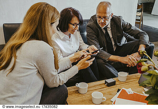 Female and male investors discussing over smart phone with hacker at startup company