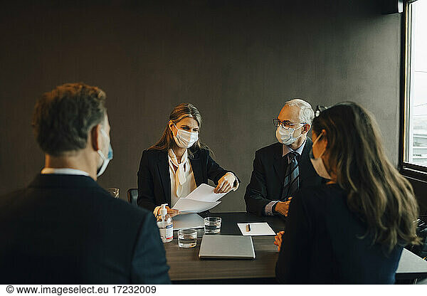 Female and male professionals brainstorming over document in board room during pandemic