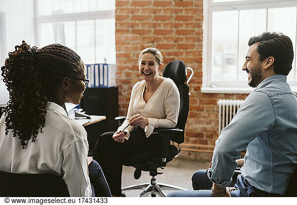 Female and male professionals laughing while discussing in office
