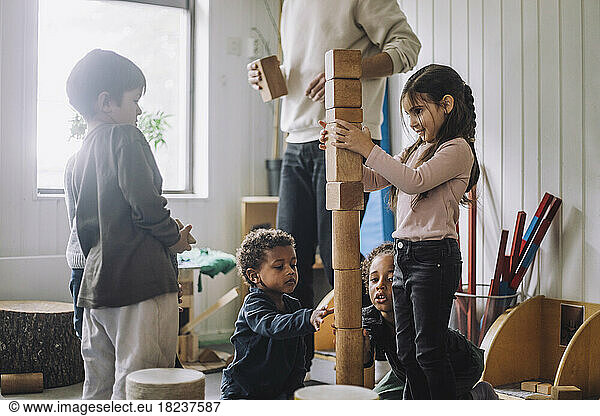 Female and male students stacking wooden toy blocks by male teacher in day care center
